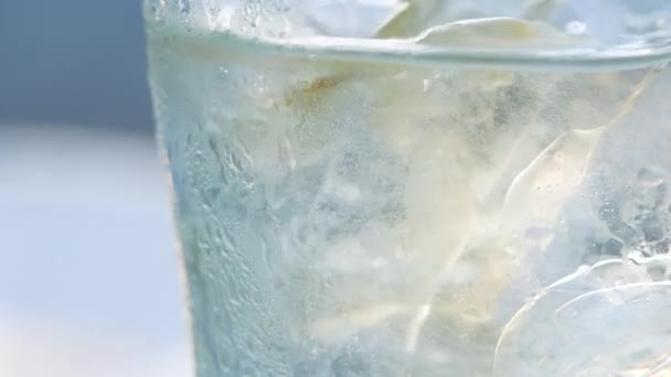 Gros plan sur la bulle d'air tout en versant de l'eau minérale carbonatée avec de la glace dans du verre sur fond vert bokeh nature.