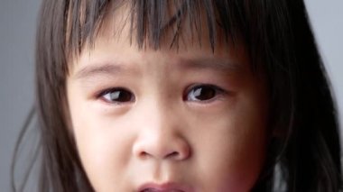 Asyalı küçük bir kızın portresi. Koyu arkaplanda üzgün bir ifade var..