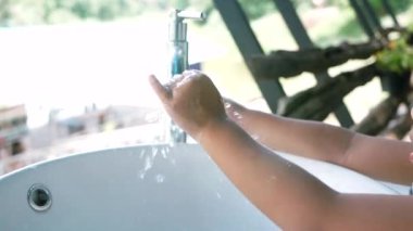 Küçük Asyalı kız su altında ellerini yıkıyor lavaboda Coronavirus 'un yayılmasını engellemek için..