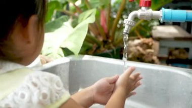 Küçük Asyalı kız su altında ellerini yıkıyor lavaboda Coronavirus 'un yayılmasını engellemek için..