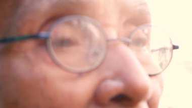 Güneşli bir bahçede, doğal bir bokeh arka planına sahip boş oturan, gözlüklü yaşlı bir adamın gözleri. seçici odak.