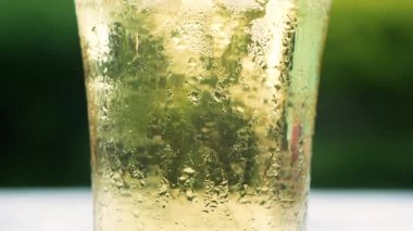 Bardağın kenarına tünemiş temiz bir bardak ve su buharına mineral karbonatlı su dökerken hava kabarcığına yakın çekim. yeşil doğa bokeh arkaplan.