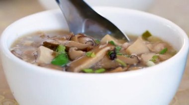 Yakın plan insan eli kaşıkla kaynamış pirinci domuz eti, shiitake mantarı ve sebzelerle dolu bir masada kepçeyle temizler..