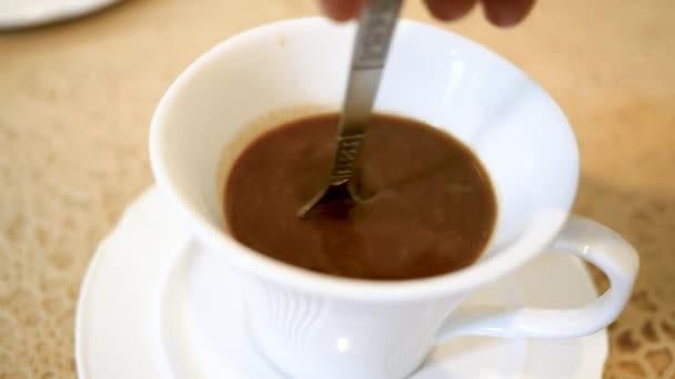 木製のテーブルの背景に白いカップにスプーンでコーヒーを攪拌人の手のクローズアップ — ストック動画
