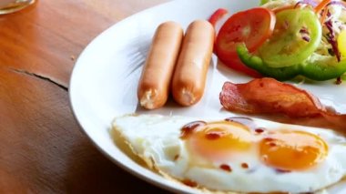 Kahvaltı yapan biri. Kızarmış yumurtalı Amerikan usulü kahvaltı, ızgara pastırma, sosis ve sebze salatası. Sağlıklı gıda konsepti.