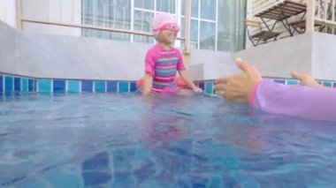 Neşeli Asyalı küçük kız çocuğu yaz günü annesiyle yüzme havuzunda oynuyor. Tatilde aile hayatı.