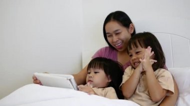 Uykulu anne ve küçük kızları geceleri yatakta tablet bilgisayar oynuyorlar. Mutlu aile zamanları..