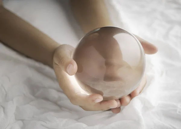 Hand holding a crystal glass ball transparent on white fabric background.