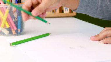 Renkli kalemle boyanmış bir elin yakın çekimi, beyaz kağıt üzerinde bir ağaç ve bulut tasviri.