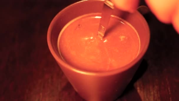 木製のテーブルの背景に黒いカップにスプーンでコーヒーを攪拌人の手のクローズアップ — ストック動画