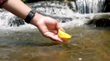 Kadının elini kapat kağıt tekneyi suya koy ve suyun arka planındaki yansıma günışığıyla uzaklaştır, tıpkı çocukluğundaki gibi..