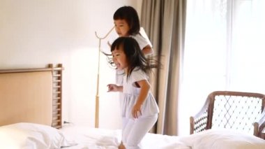 Beyaz pijamalı iki küçük kardeş yatak odasında birlikte yatağa atlarken eğleniyorlar. Çocukluk mutluluğu kavramı.