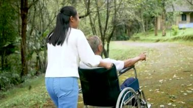 Mutlu büyükbaba tekerlekli sandalyede rahatlıyor ve torunuyla parkta yürüyor. Aile mutlu bir yaşam tarzı.