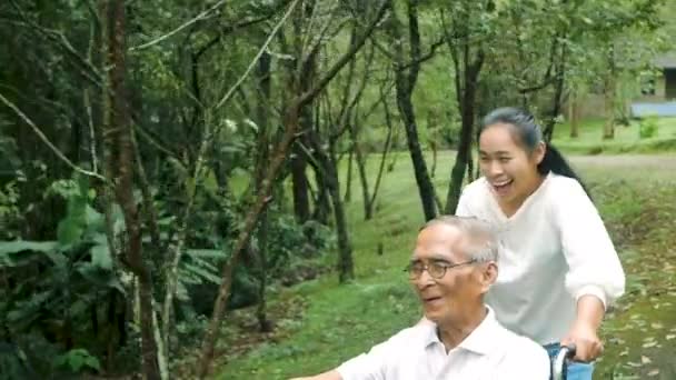 車椅子で幸せな笑顔の祖父がリラックスして公園の孫娘の屋外で歩いています 家族の幸せな生活 — ストック動画