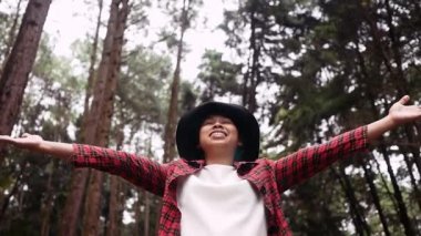 Çam ormanında el kaldırmış ve tatilde doğanın tadını çıkaran genç bir kadın..