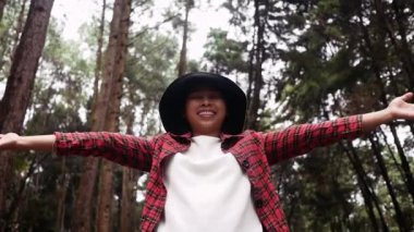 Çam ormanında el kaldırmış ve tatilde doğanın tadını çıkaran genç bir kadın..