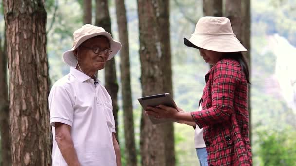 散歩中のお父さんと一緒に大人の娘と一緒にデジタルタブレットを手に森の中で話しています 森林破壊から木を守る人々との地球の日の概念 — ストック動画