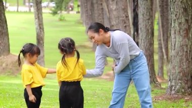Mutlu anne ve çocuklar bahçede yeşil çimlerde oturup oynuyorlar. Rahatlama zamanı ve aile ilişkisi kavramları.