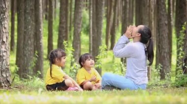 Mutlu anne ve çocuklar bahçede yeşil çimlerde oturup oynuyorlar. Rahatlama zamanı ve aile ilişkisi kavramları.