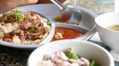 Kadının ellerinin kaşıkla ve çatalla domuz budu yiyerek, soslu ve tatlı soslu pilavı tabağa koyarak yakın çekimi. Lezzetli Tayland yemekleri..