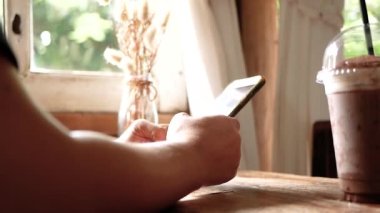 Asyalı kadının sosyal medyayı okurken ve tatilde kafede telefonla yazarken yan görüntüsü. Eller yakın çekim.