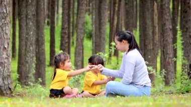 Mutlu anne ve çocuklar bahçede yeşil çimlerde oturup oynuyorlar. Rahatlama zamanı ve aile ilişkisi kavramları.