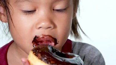 Yakından bakınca tatlı çörek yiyen ve beyaz arka planda tadını çıkaran küçük tatlı bir kız görüyorum..