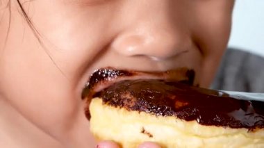 Yakından bakınca tatlı çörek yiyen ve beyaz arka planda tadını çıkaran küçük tatlı bir kız görüyorum..