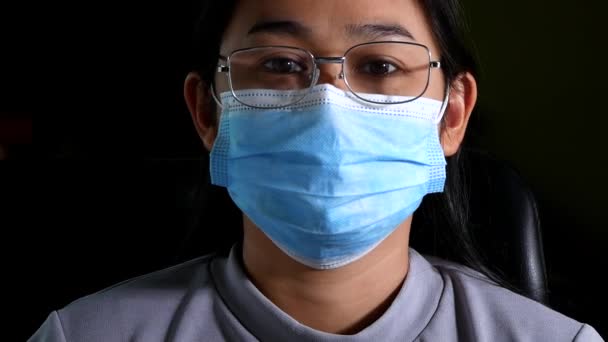 暗い背景でコロナウイルスの流行 Pm20 大気汚染 から彼女を守るために医療面のマスクを身に着けて 眼鏡をかけた自信アジアの女性の肖像画を閉じます 新しい正常な行動 — ストック動画
