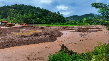Enkaz ve ağır makinelerle dolu çamurlu bir nehir akıntısı kurtarma çabaları üzerinde çalışıyor..
