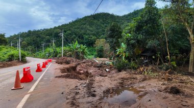 Şiddetli yağmurun ardından güvenlik için koni ve bariyerler konan sel ve heyelan ile aşınmış hasarlı bir dağ yolu.