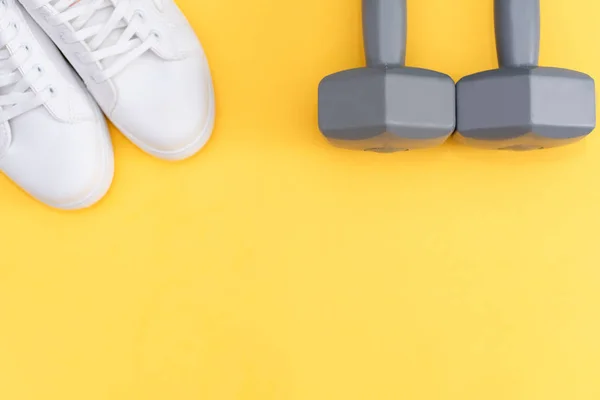 Fitness accessories on a yellow background. Sneakers, bottle of water, earphones and dumbbells.