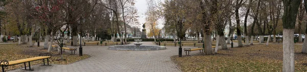 Широкий тихий осенний парк с мраморным фонтаном и металлическими скамейками — стоковое фото