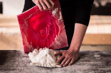The sculptor works in a plaster workshop. Separates the silicone mold from the plaster sculpture of the lions head. clipart