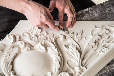 Heykeltraşın elleri aletle. Heykeltıraş stüdyoda çalışıyor. Alçıdan dekoratif bir element yaratmak. Barok tarzında lüks bir sıva. Kapatın. Seçici odak.