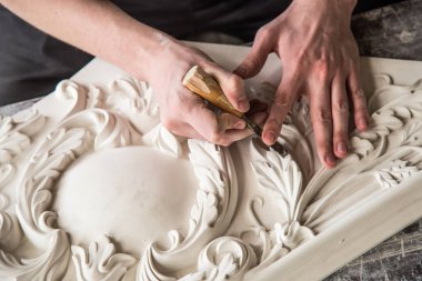 Heykeltraşın elleri aletle. Heykeltıraş stüdyoda çalışıyor. Alçıdan dekoratif bir element yaratmak. Barok tarzında lüks bir sıva. Kapatın. Seçici odak.
