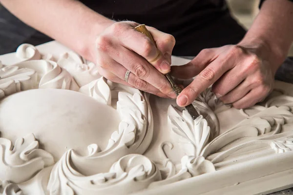 Hands of the sculptor with the tool. The sculptor works in the Studio. Creation of a decorative element from plaster. Luxurious stucco in Baroque style. Close up. Selective focus.