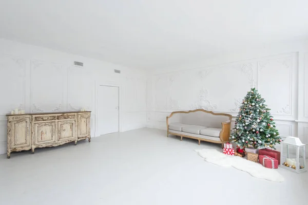 Lujoso interior brillante con paredes de estuco, árbol de Navidad, cómoda vintage y sofá . — Foto de Stock