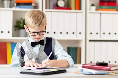 Süveter giyen sarışın okul çocuğu sınıf ödevi yapıyor.