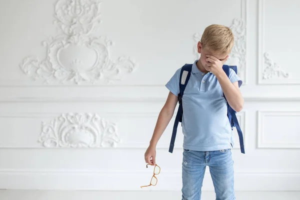 Un niño en una camiseta azul y los vaqueros se quitan las gafas y frotan los ojos. Fotos De Stock Sin Royalties Gratis