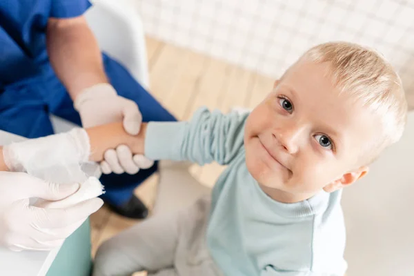 Doctor in blauw uniform maken elastische verbonden rond een jongen hand met trauma in zijn arm. in het ziekenhuis — Stockfoto