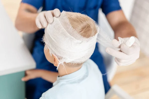 Sport letsel. Arts maakt bandage op hoofd patiënt, in het ziekenhuis. — Stockfoto