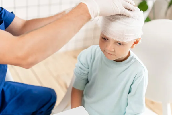 Doctor verbonden een jongen hoofd met trauma in zijn hoofd en elastische verbonden rond zijn hoofd — Stockfoto