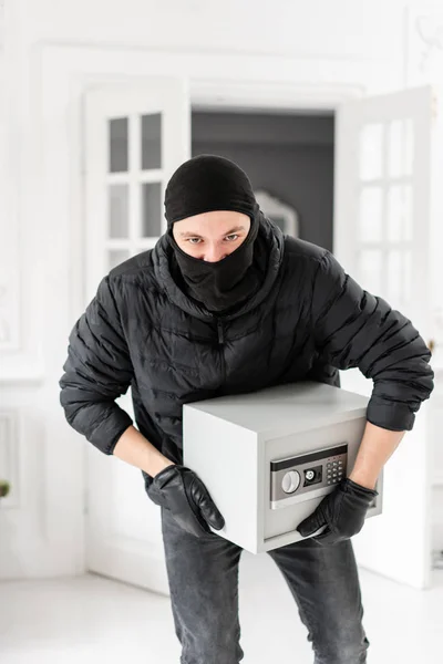 Tolvaj nézi a kamerát, fekete Balaclava lopás modern elektronikus biztonságos dobozban. A betörő bűncselekményt követ el luxus apartman stukkók. — Stock Fotó