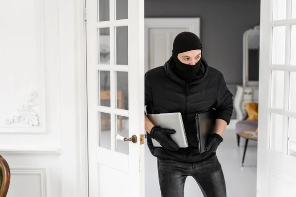 Siyah balaclava ile hırsız iki modern pahalı dizüstü bilgisayarlar çalmak. Hırsız sıva ile lüks dairede bir suç işler.