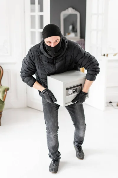 Tjuv tittar på kameran med svart Balaclava stjäla modern elektronisk Safe box. Inbrottstjuv begår ett brott i Lyxlägenhet med stuckatur. — Stockfoto