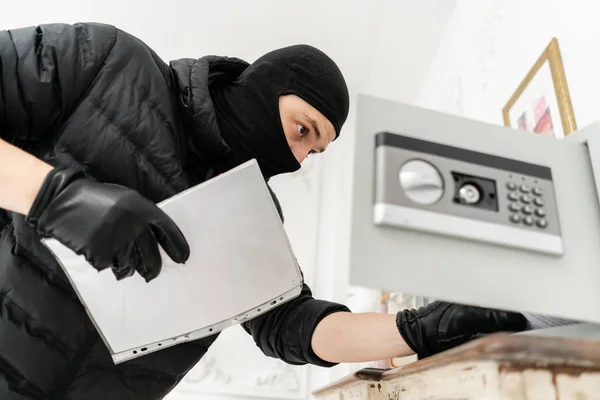 O ladrão abre o cofre electrónico. O ladrão comete um crime em apartamento de luxo com estuque. Ladrão com balaclava preta roubando cofre . — Fotografia de Stock