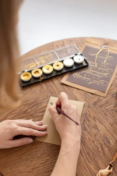 Eine Kalligraphin hält vor Arbeitsbeginn einen Stift mit Tinte vor eine leere Postkarte. Weicher Fokus. — Stockfoto