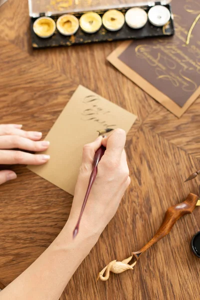 Die attraktive Kalligraphin hält einen Stift mit Tinte in der Hand und signiert eine Karte in handgeschriebener Schrift. Nahaufnahme. Weicher Fokus. — Stockfoto