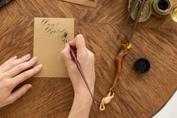 Kalligraph hält einen Stift mit Tinte in der Hand. schreibt das Mädchen einen Brief in handgeschriebener Schrift. Kreativwerkstatt des Künstlers. Weicher Fokus. — Stockfoto